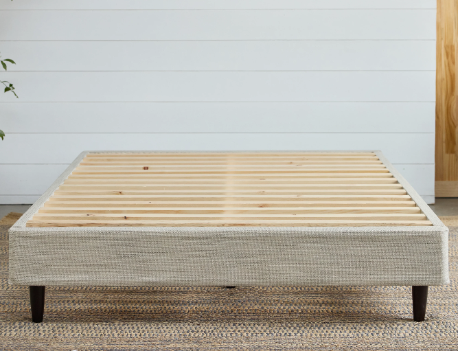 A picture of the Avocado Foundation with legs standing on dark brown legs inside of a bedroom. You can clearly see the wooden slats that are used to support any mattress that is placed on top of it.  The foundation with legs has a clean, modern design, and is easy to put together with tool-free assembly. 